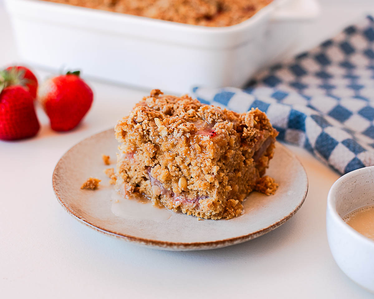 Strawberry coffee cake slice on plate with glaze and baking dish in background