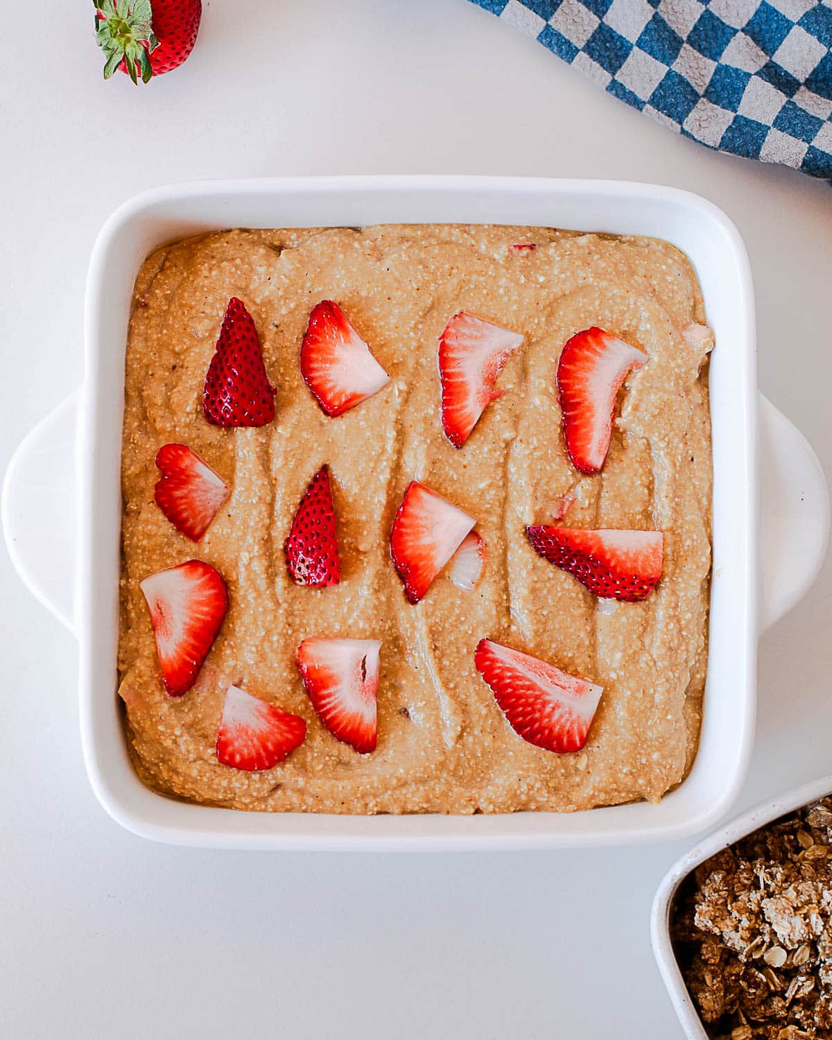 Strawberry coffee cake batter spread in a square baking dish with sliced strawberries on top