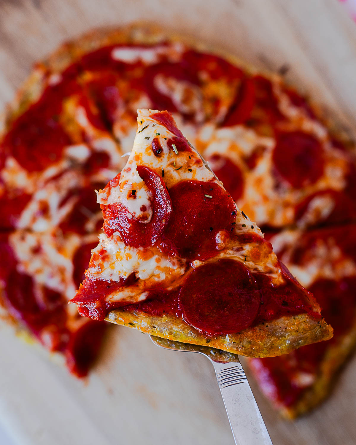 Slice of pepperoni chicken crust pizza lifted from the pizza board with melted mozzarella and pepperoni.