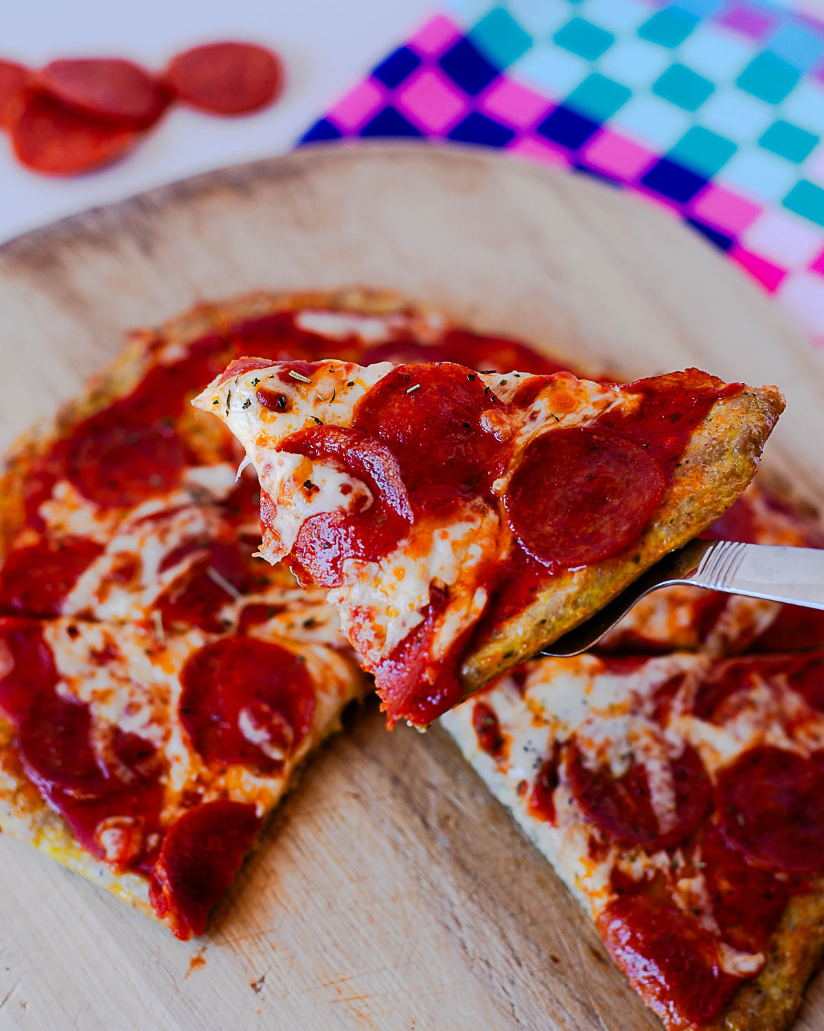 Close-up of a slice of high protein pepperoni chicken crust pizza on a serving spatula.