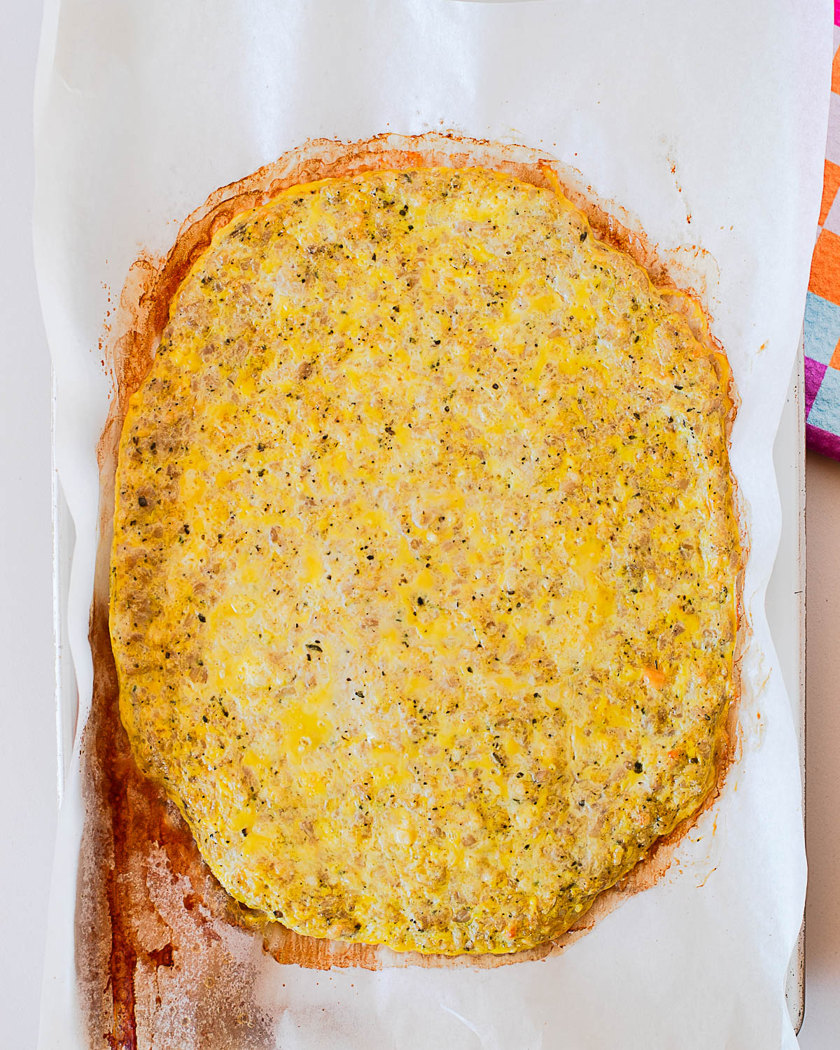 Baked chicken crust pizza before toppings with golden edges on parchment paper.