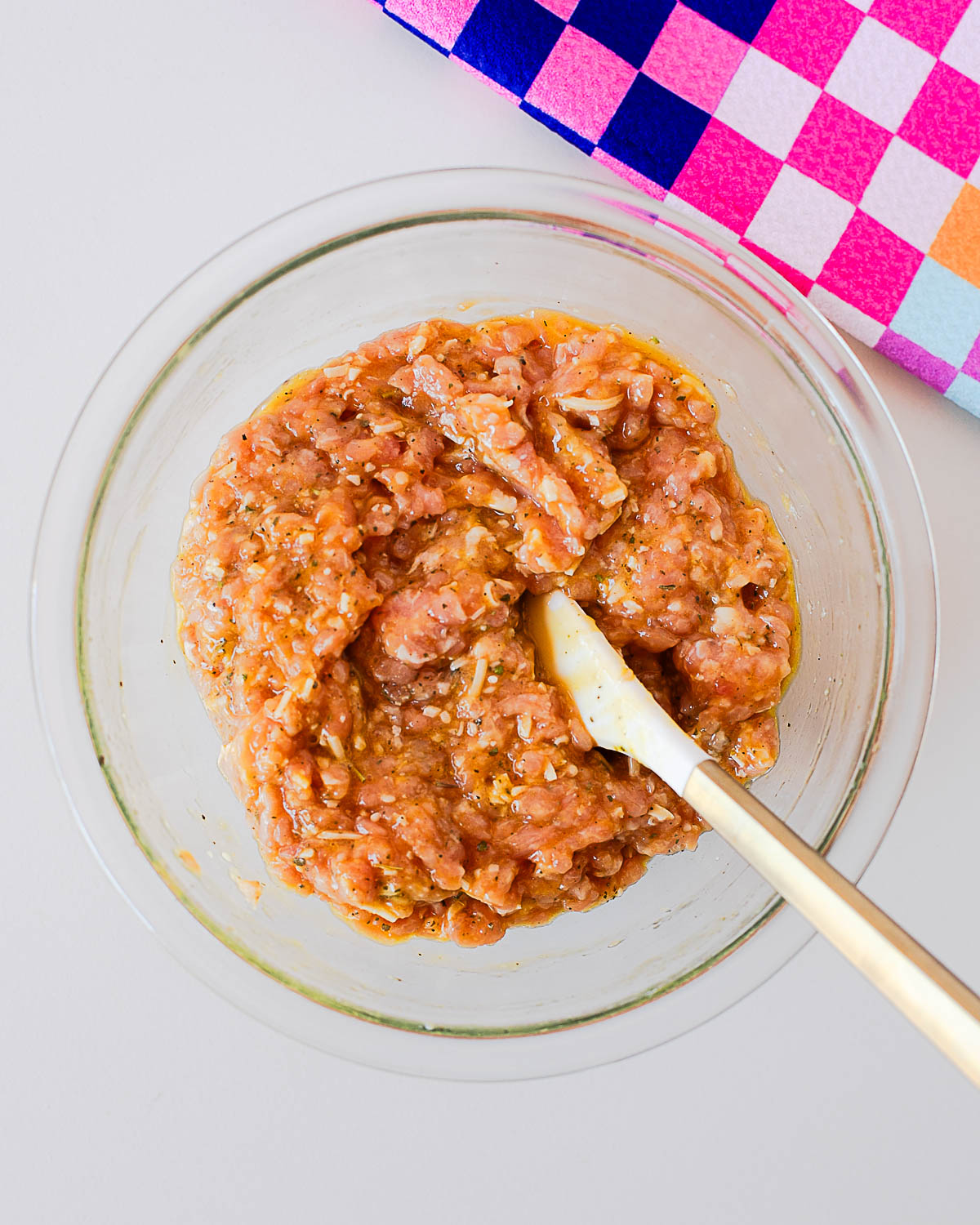 Ground chicken mixed with eggs, parmesan cheese, and seasonings in a glass bowl for chicken crust pizza.