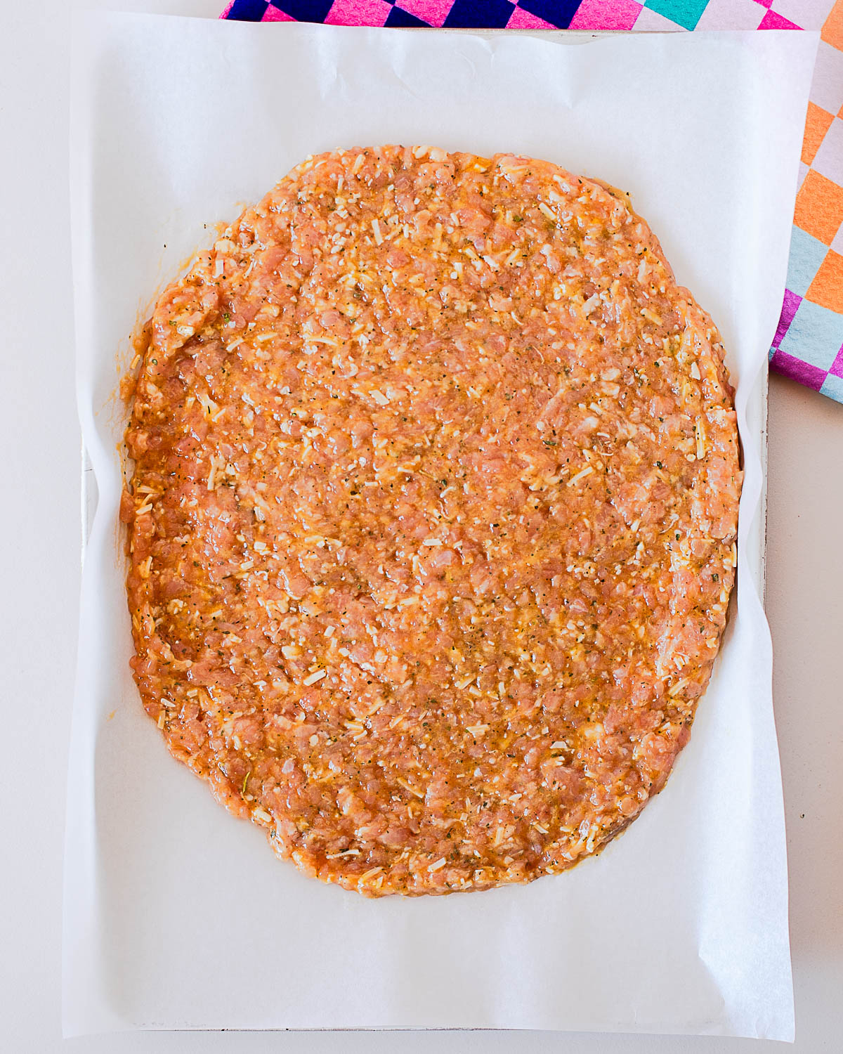 Raw chicken crust pizza mixture spread thinly onto parchment paper on a baking sheet before baking.