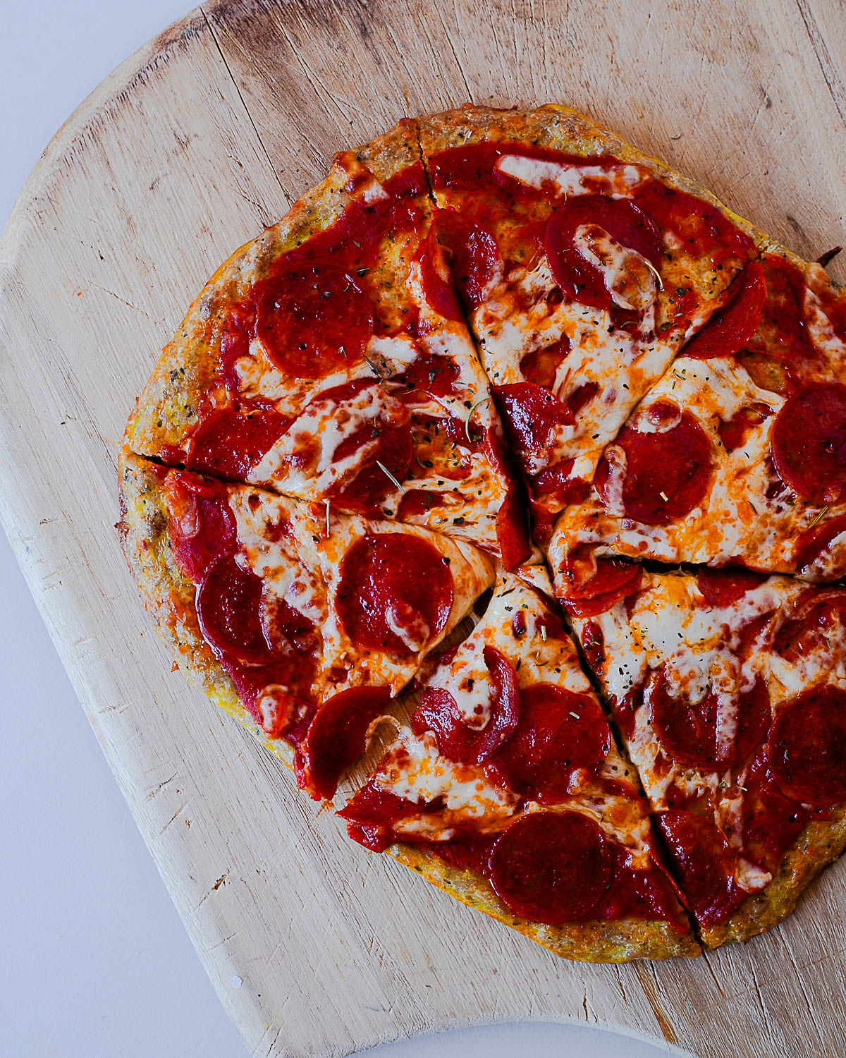 High protein pepperoni chicken crust pizza sliced on a wooden pizza board.
