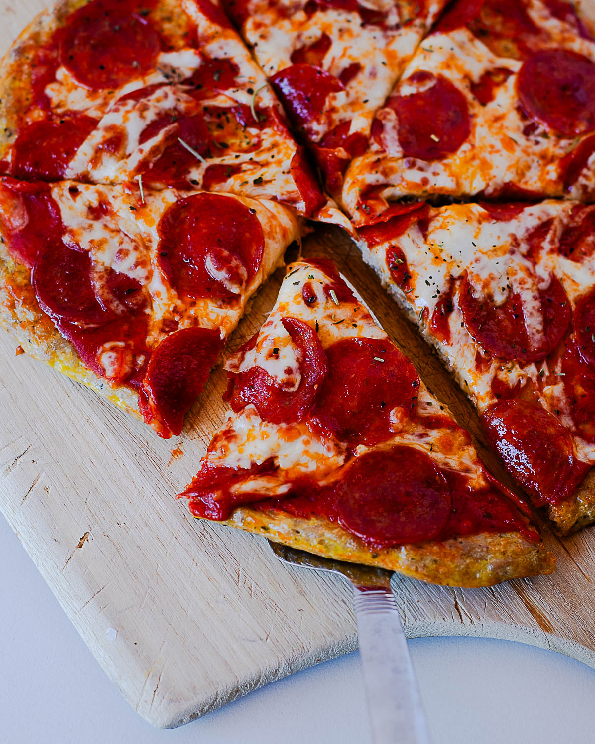 Close-up of sliced pepperoni chicken crust pizza on a wooden pizza board.