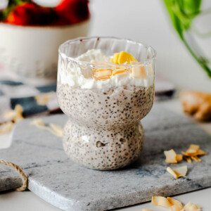 Creamy coconut chia pudding breakfast topped with Greek yogurt and toasted coconut flakes in a textured glass dessert cup.