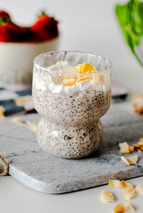 Creamy coconut chia pudding breakfast topped with Greek yogurt and toasted coconut flakes in a textured glass dessert cup.