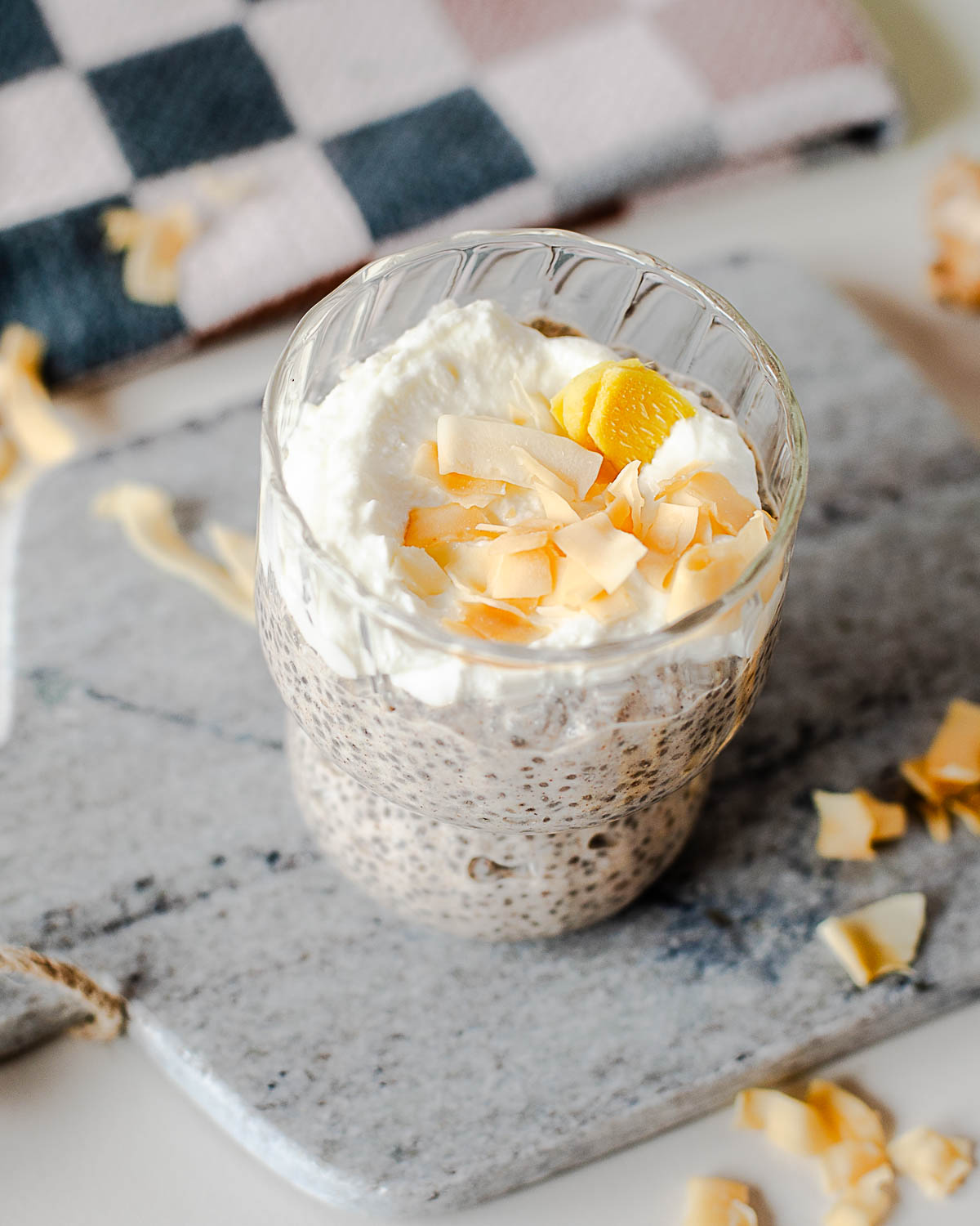Coconut chia pudding with chia seeds, Greek yogurt, and toasted coconut flakes in a glass dessert cup with cozy breakfast styling.