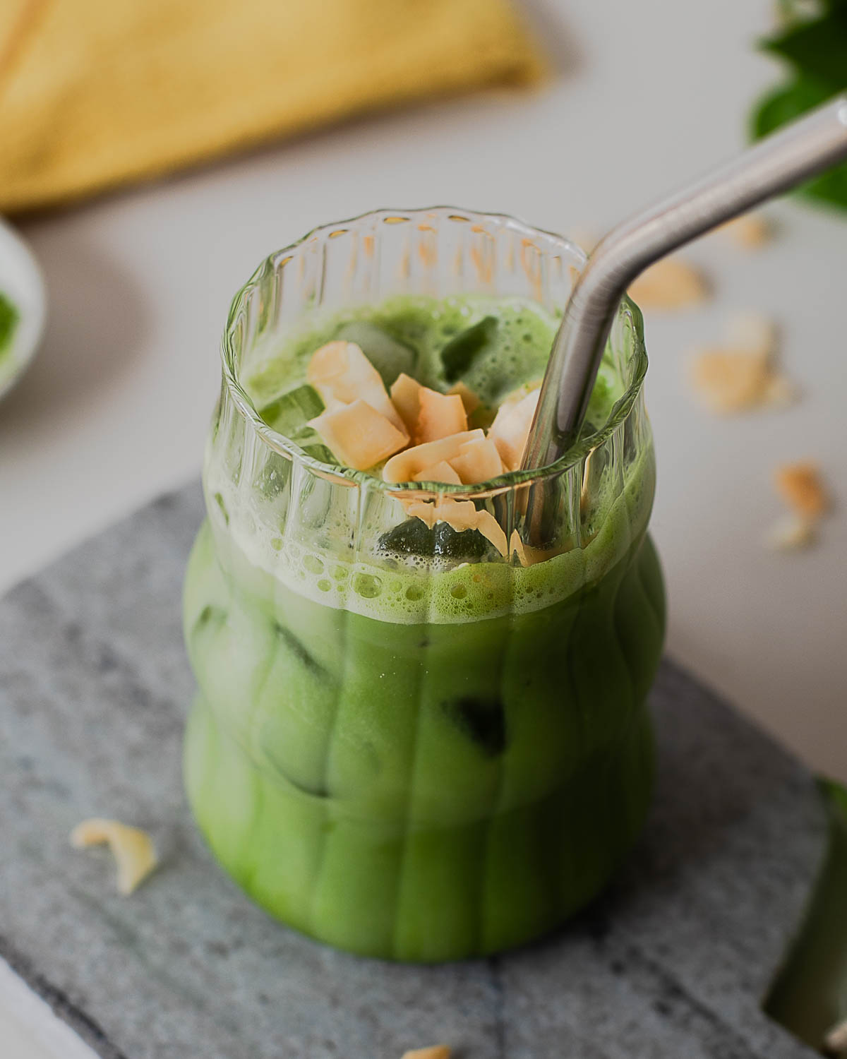 Stainless steel straw in a creamy iced coconut protein matcha latte topped with toasted coconut flakes.