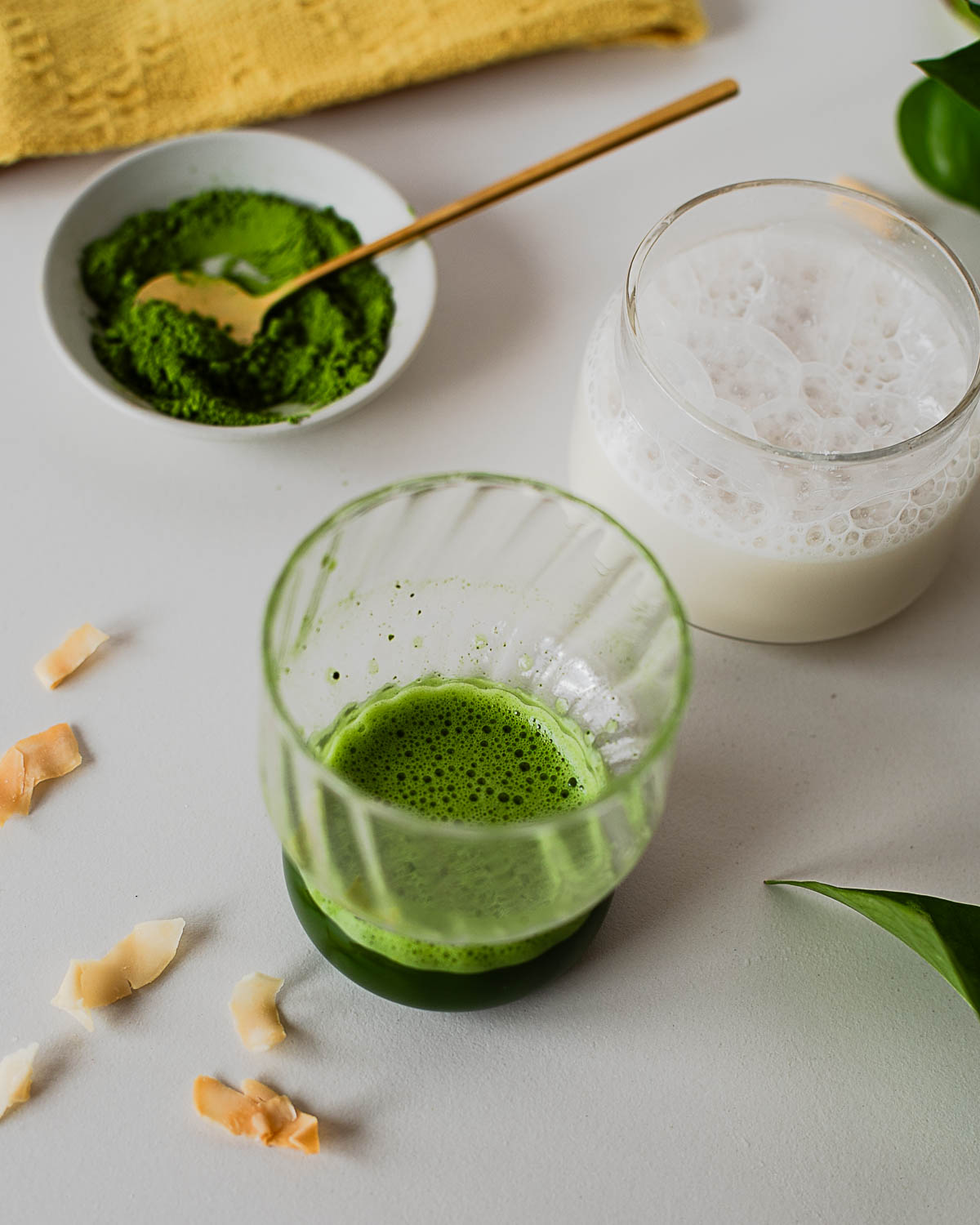 Matcha powder whisked with hot water beside frothy coconut protein milk for an iced coconut protein matcha latte recipe.