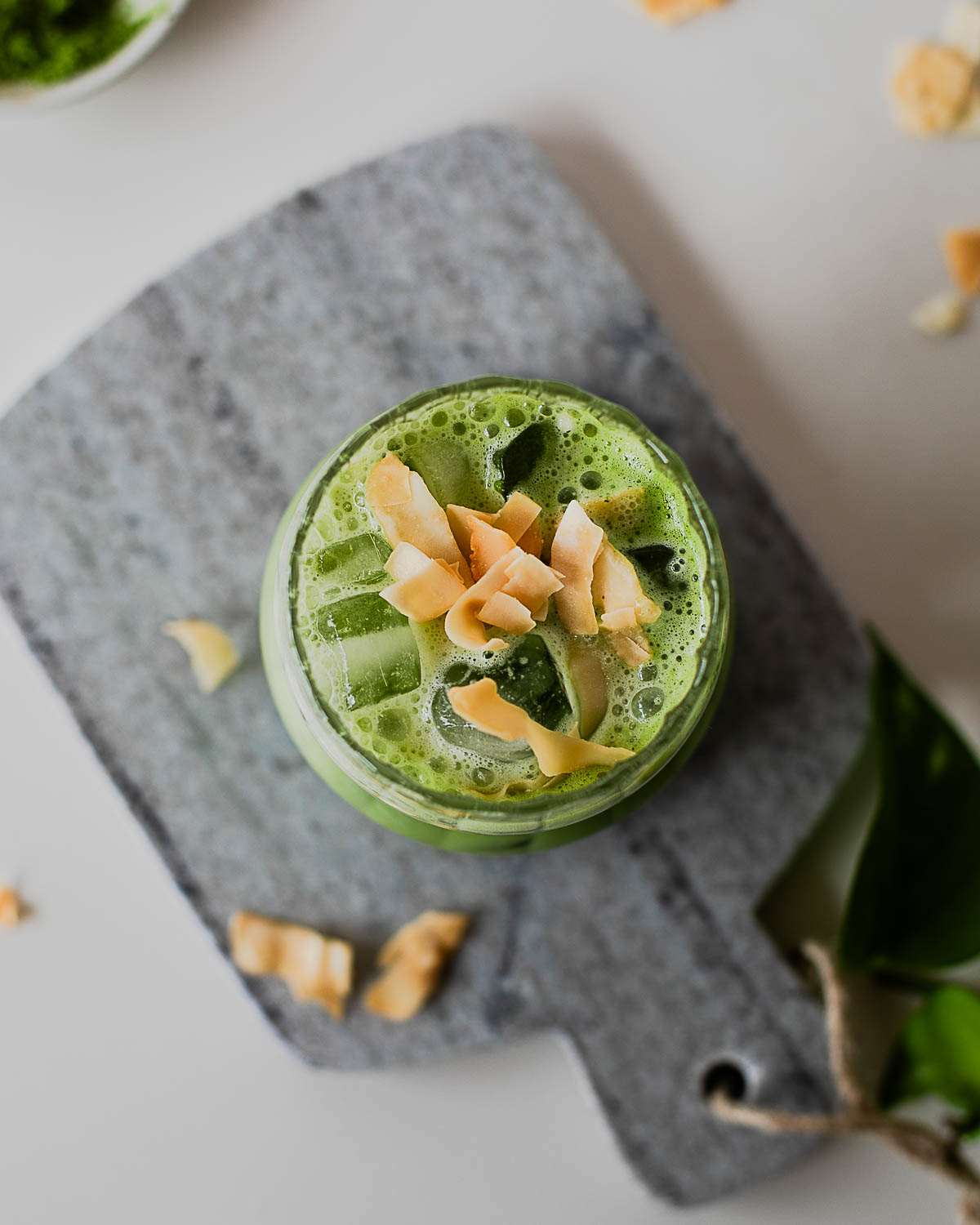 Overhead shot of an iced coconut matcha latte with creamy froth, ice cubes, and toasted coconut garnish.