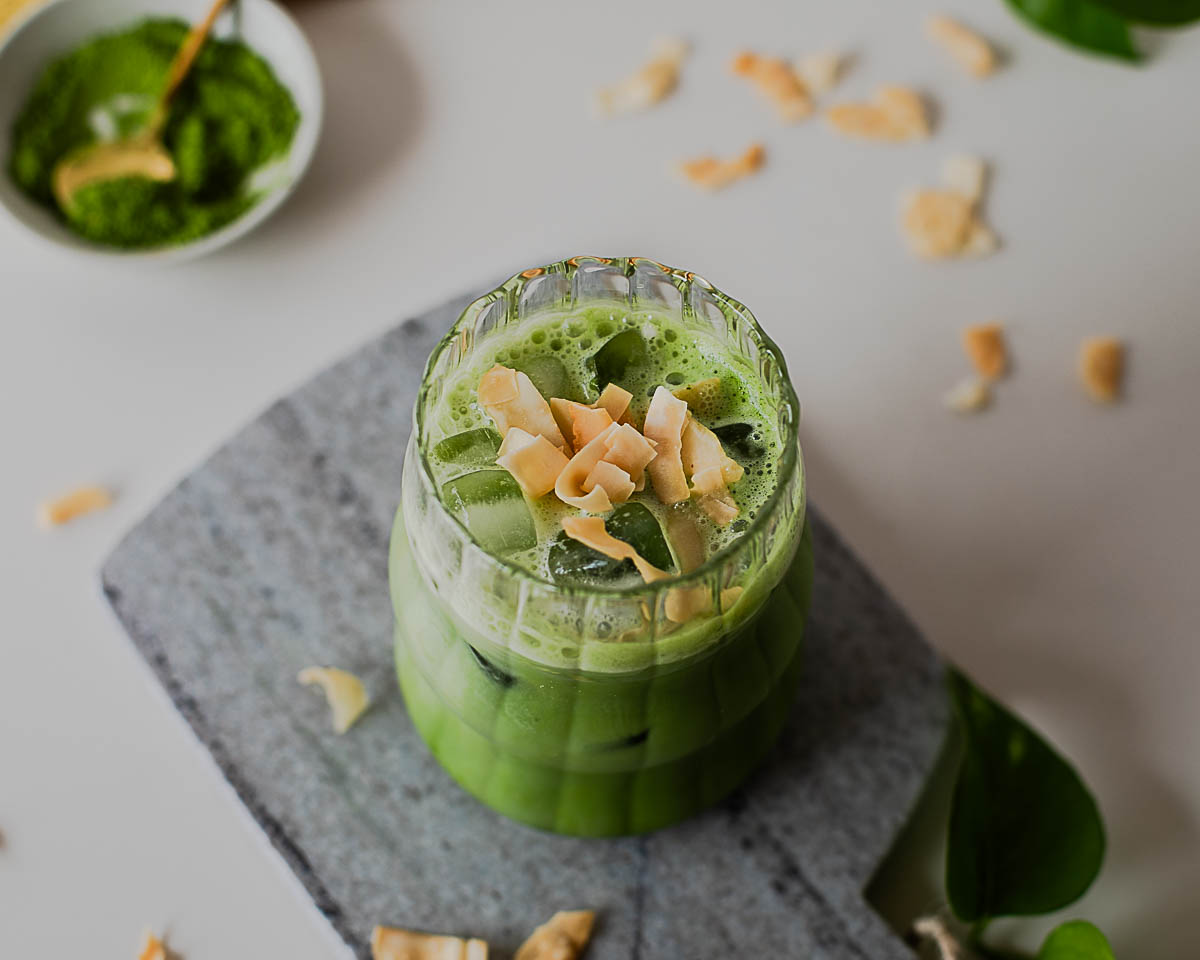 Iced coconut protein matcha latte topped with toasted coconut flakes for a creamy tropical matcha drink.