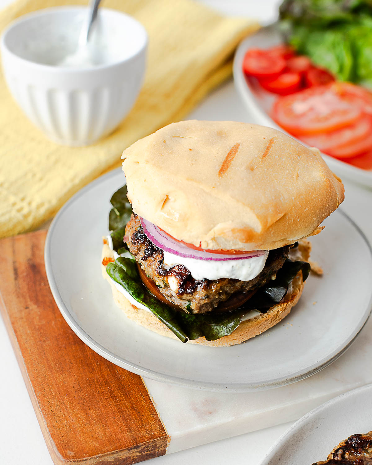 Greek-style lamb burger served on a toasted bun with lettuce, tomato, and red onion slices