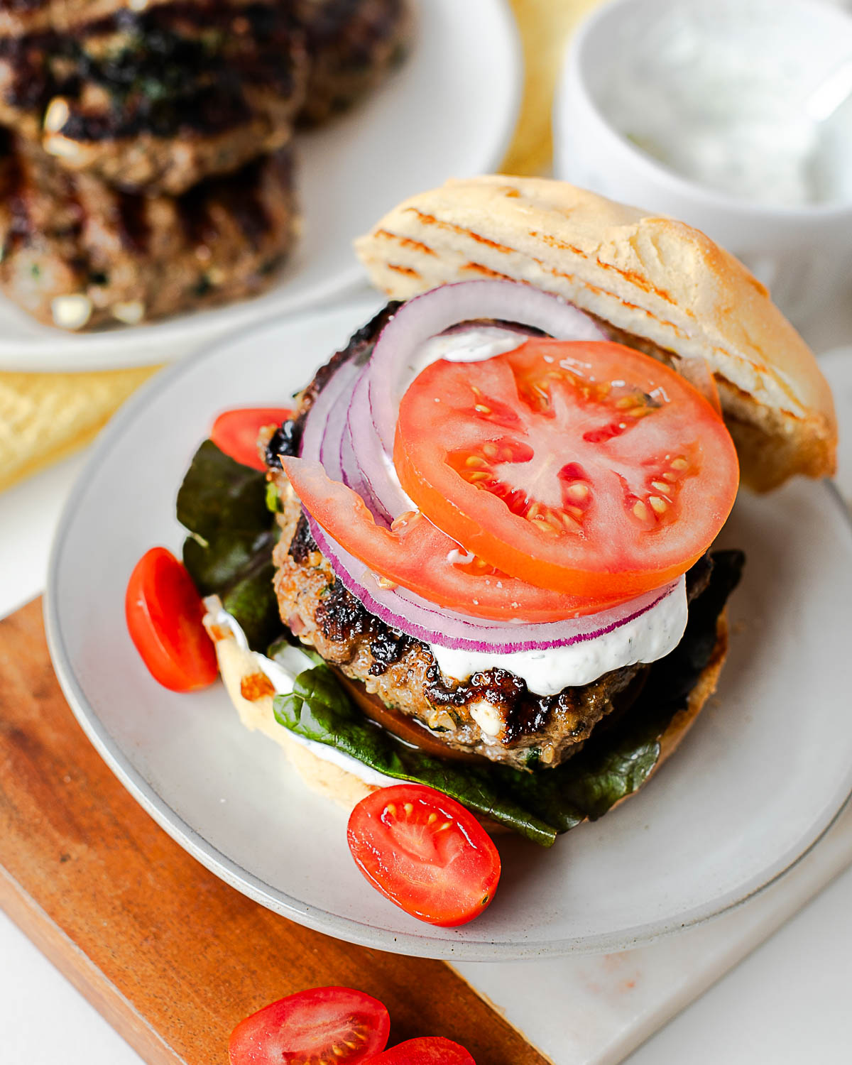 Juicy lamb burger with feta and spinach served with fresh tomato slices and creamy dill sauce