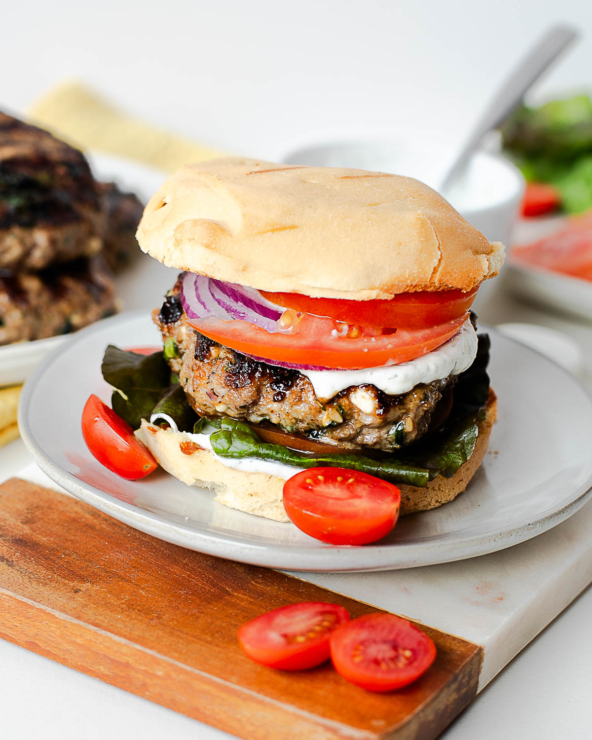 Close-up of a lamb feta burger with grilled bun, tomato slices, red onion, and yogurt sauce