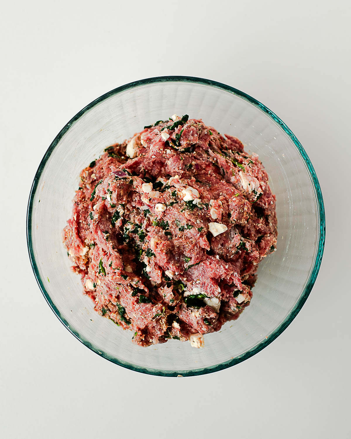 Ground lamb mixed with spinach, feta cheese, herbs, and seasonings in a glass bowl for homemade Greek lamb burgers