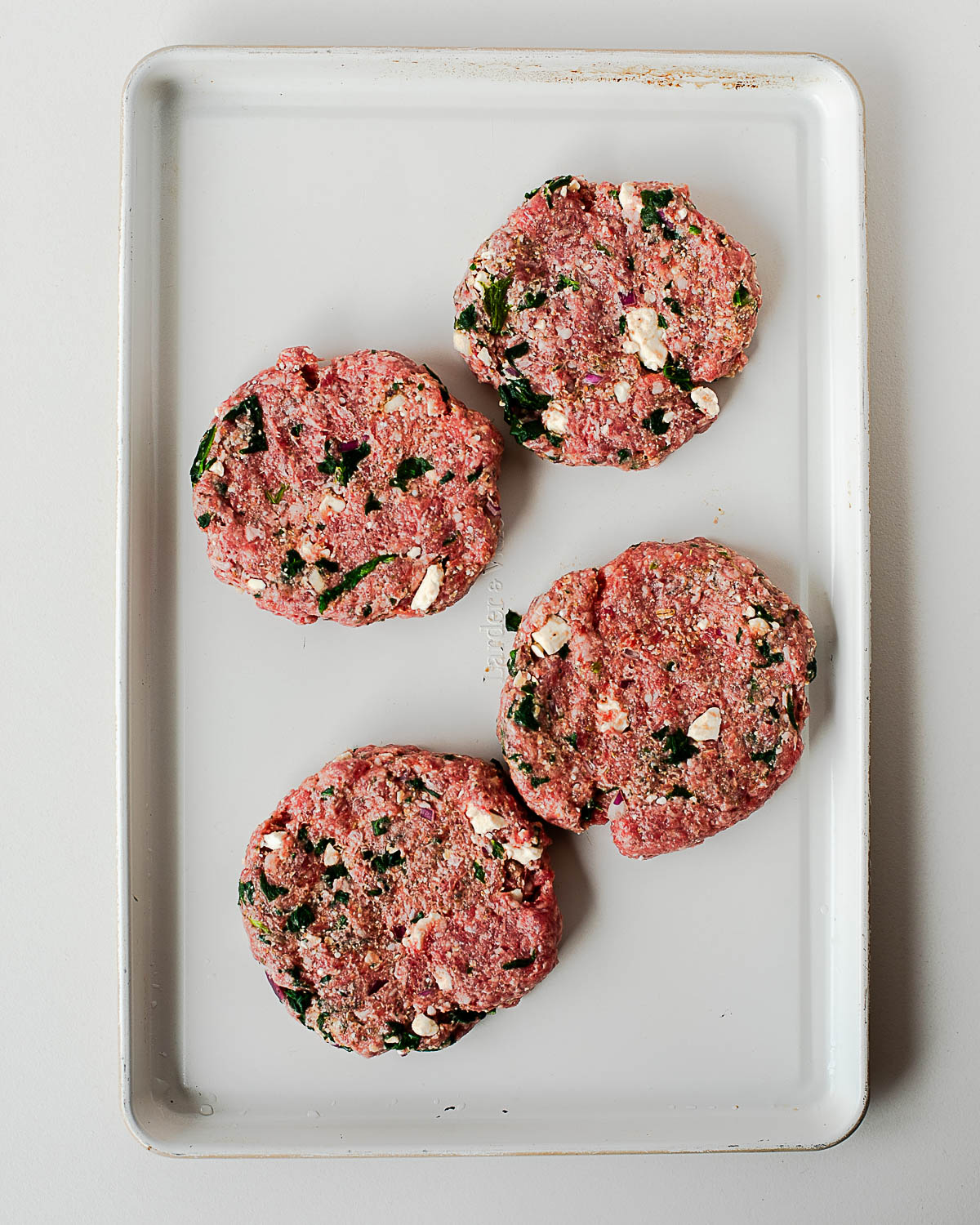 Uncooked lamb burger patties with feta and spinach shaped on a baking sheet before grilling