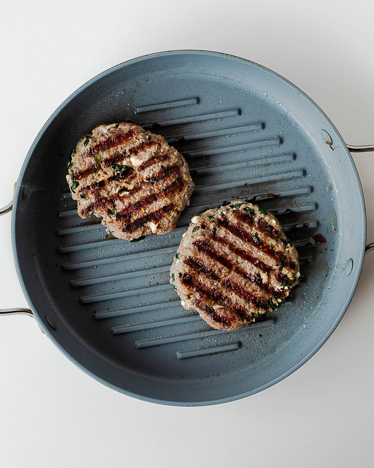 Greek lamb burger patties cooking on a grill pan with charred grill marks