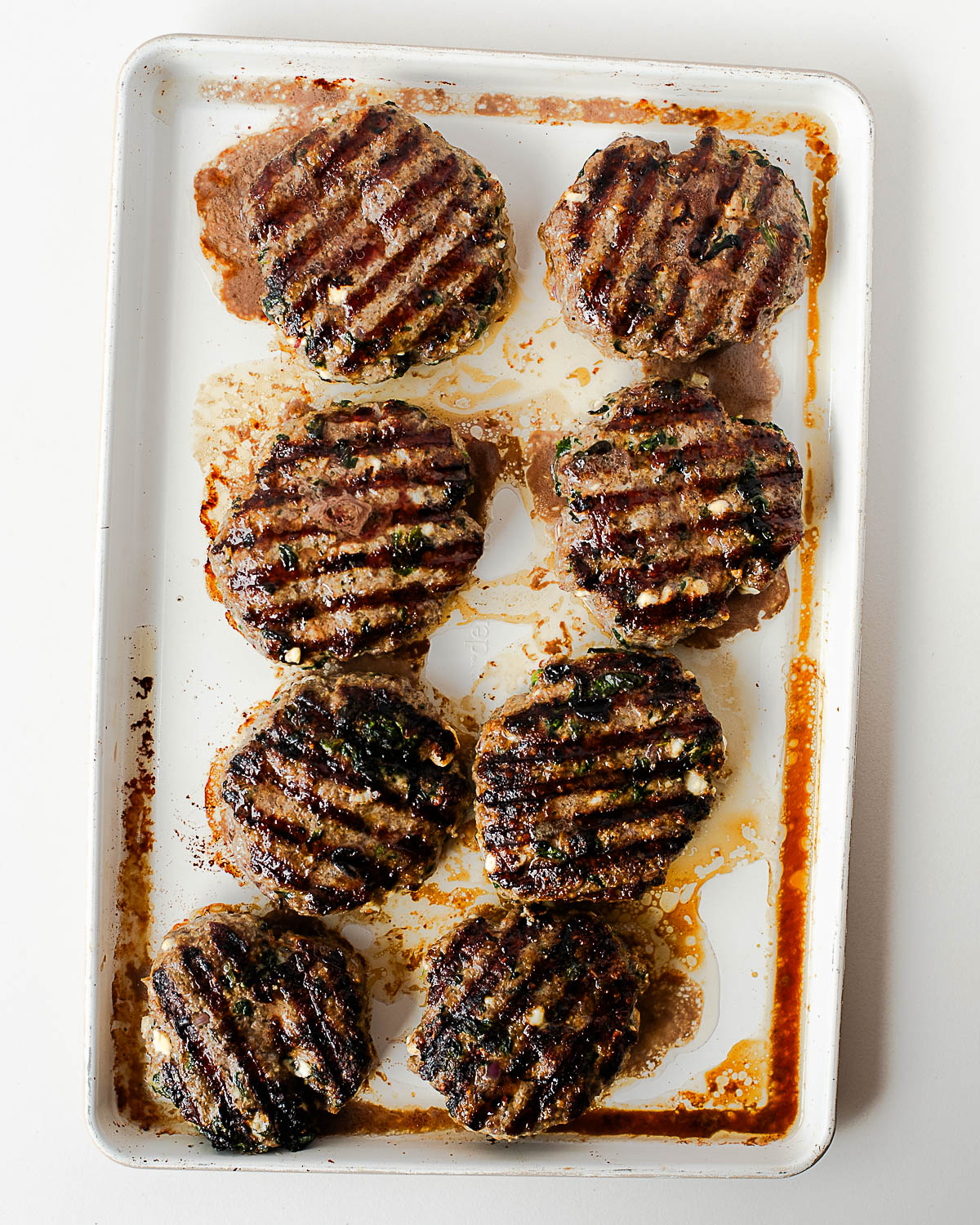 Cooked lamb burgers with feta cheese resting on a baking sheet after grilling