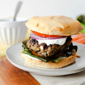 Mediterranean lamb burger topped with creamy dill yogurt sauce and fresh vegetables on a burger bun