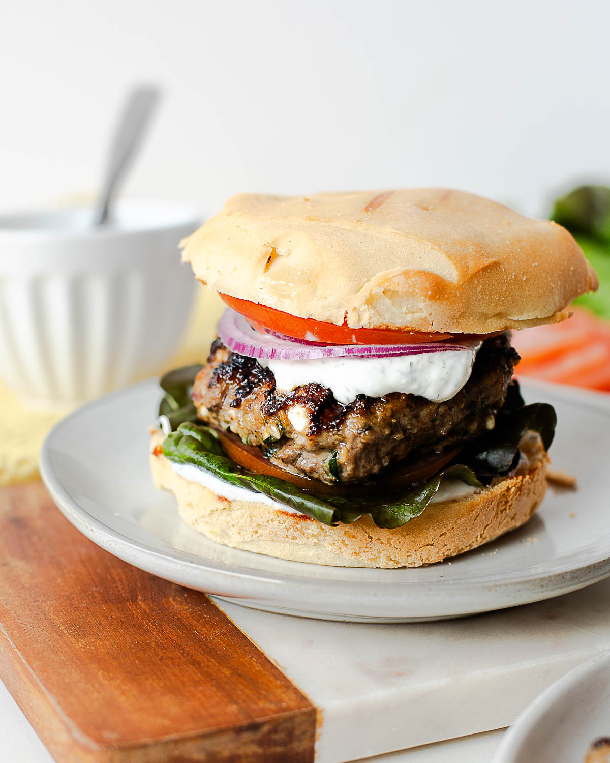Mediterranean lamb burger topped with creamy dill yogurt sauce and fresh vegetables on a burger bun