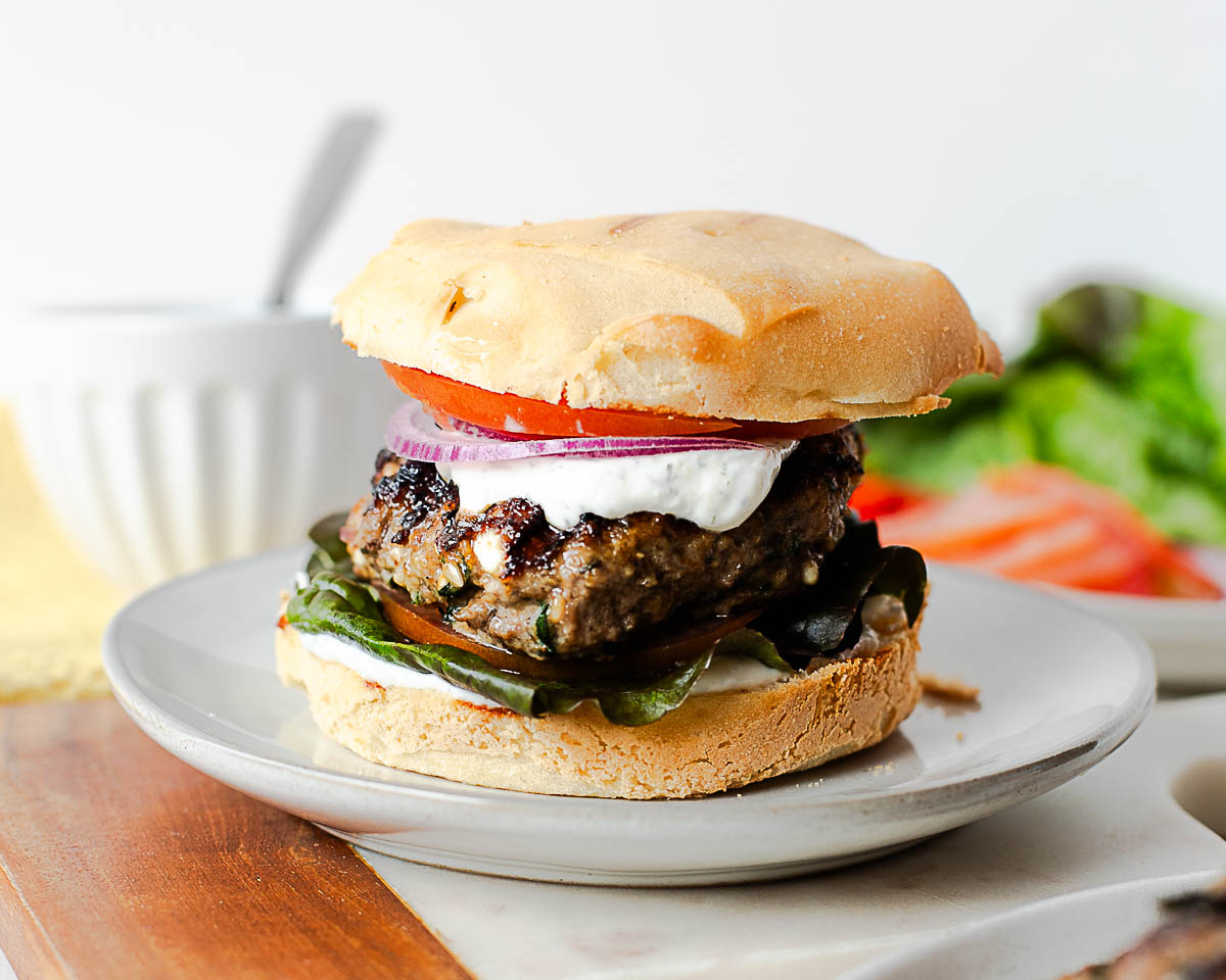 Greek lamb burger with feta yogurt sauce, lettuce, tomato, and red onion on a toasted bun