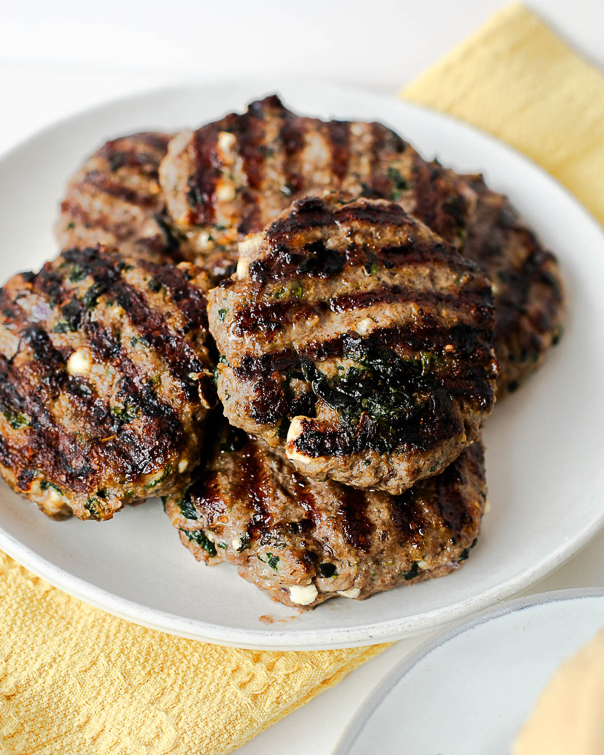 Grilled lamb burger patties stacked on a plate showing charred edges and feta throughout