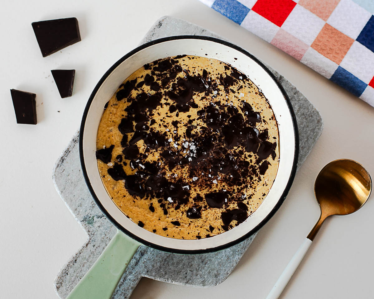 Freshly baked protein cookie skillet with melted dark chocolate and flaky sea salt in a mini cast iron skillet.
