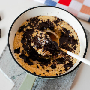 Spoon scooping into a gooey protein cookie skillet with melted dark chocolate and flaky sea salt on top.