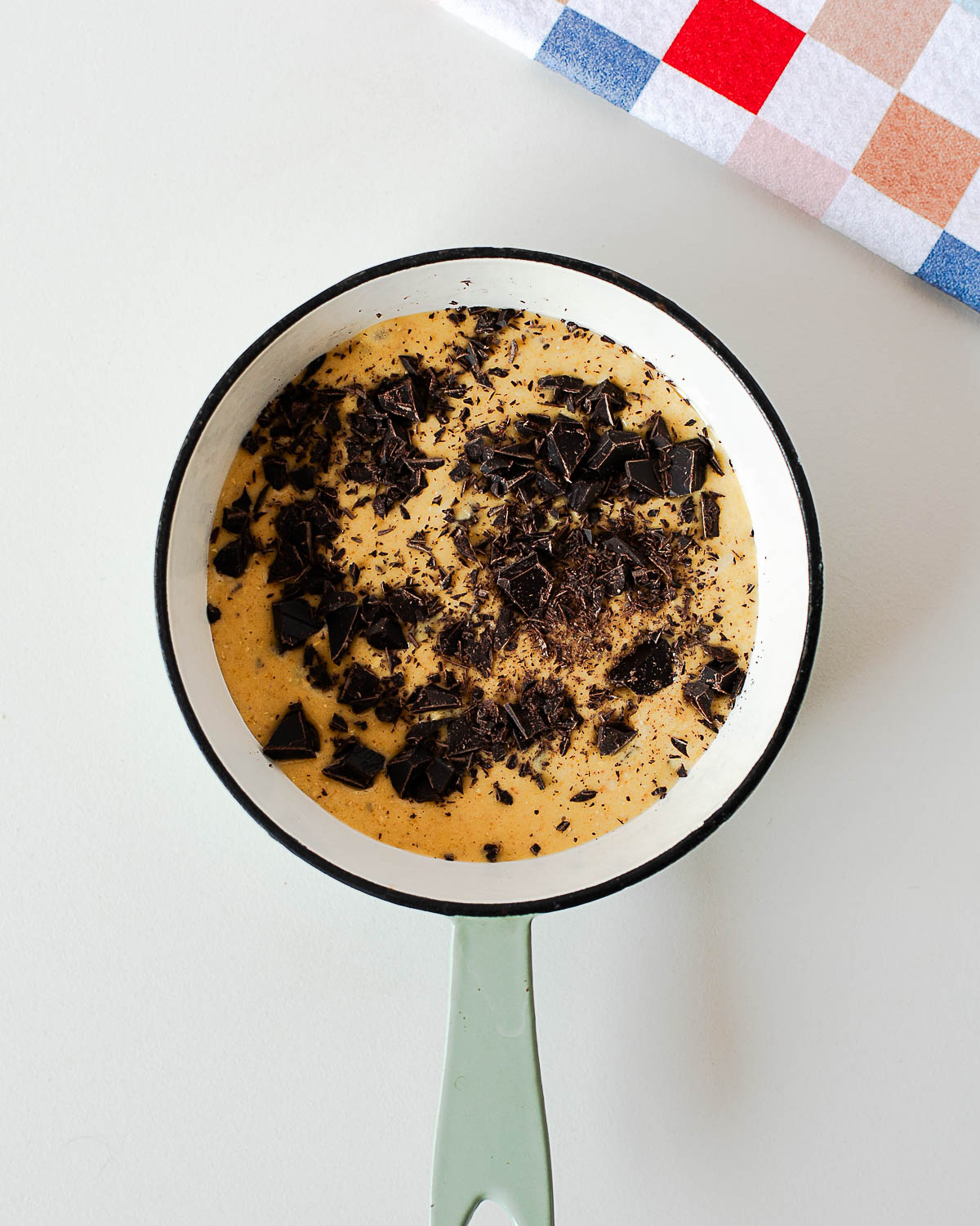 Overhead shot of single serve protein cookie skillet batter in a small white skillet with chopped dark chocolate on top before baking.