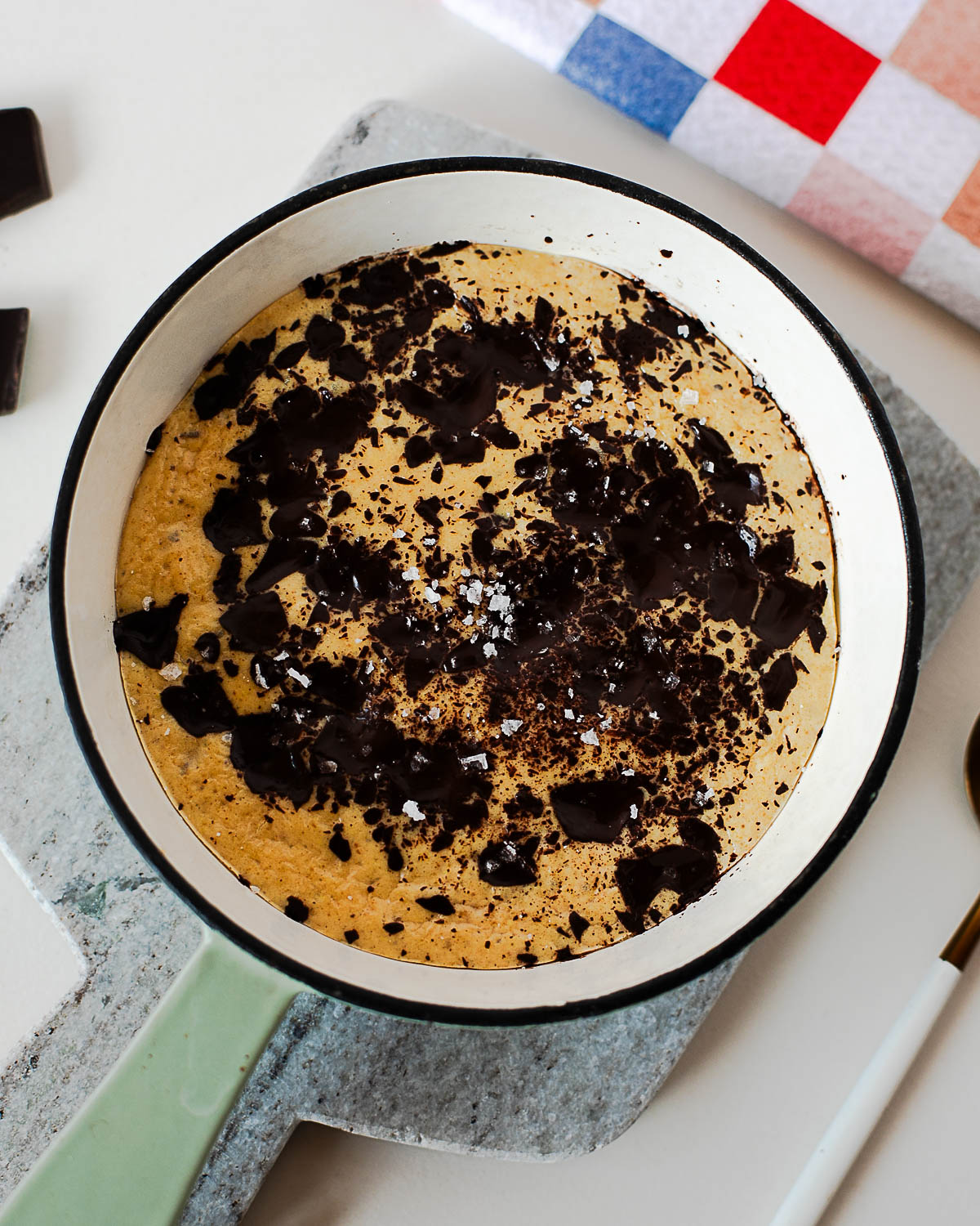 Single serve protein cookie skillet in a white enamel skillet topped with dark chocolate chunks and sea salt.