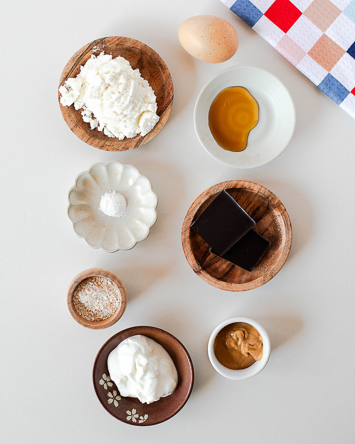 Ingredients for a protein cookie skillet including vanilla whey protein powder, Greek yogurt, oat flour, maple syrup, cashew butter, egg yolk, and dark chocolate.