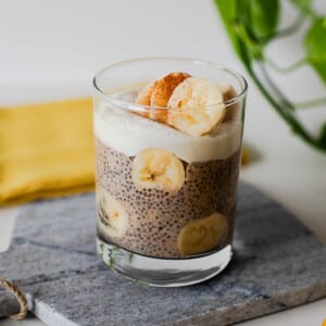 High-protein banana chia pudding with Greek yogurt topping, fresh banana slices, and cinnamon served in a clear glass dish.