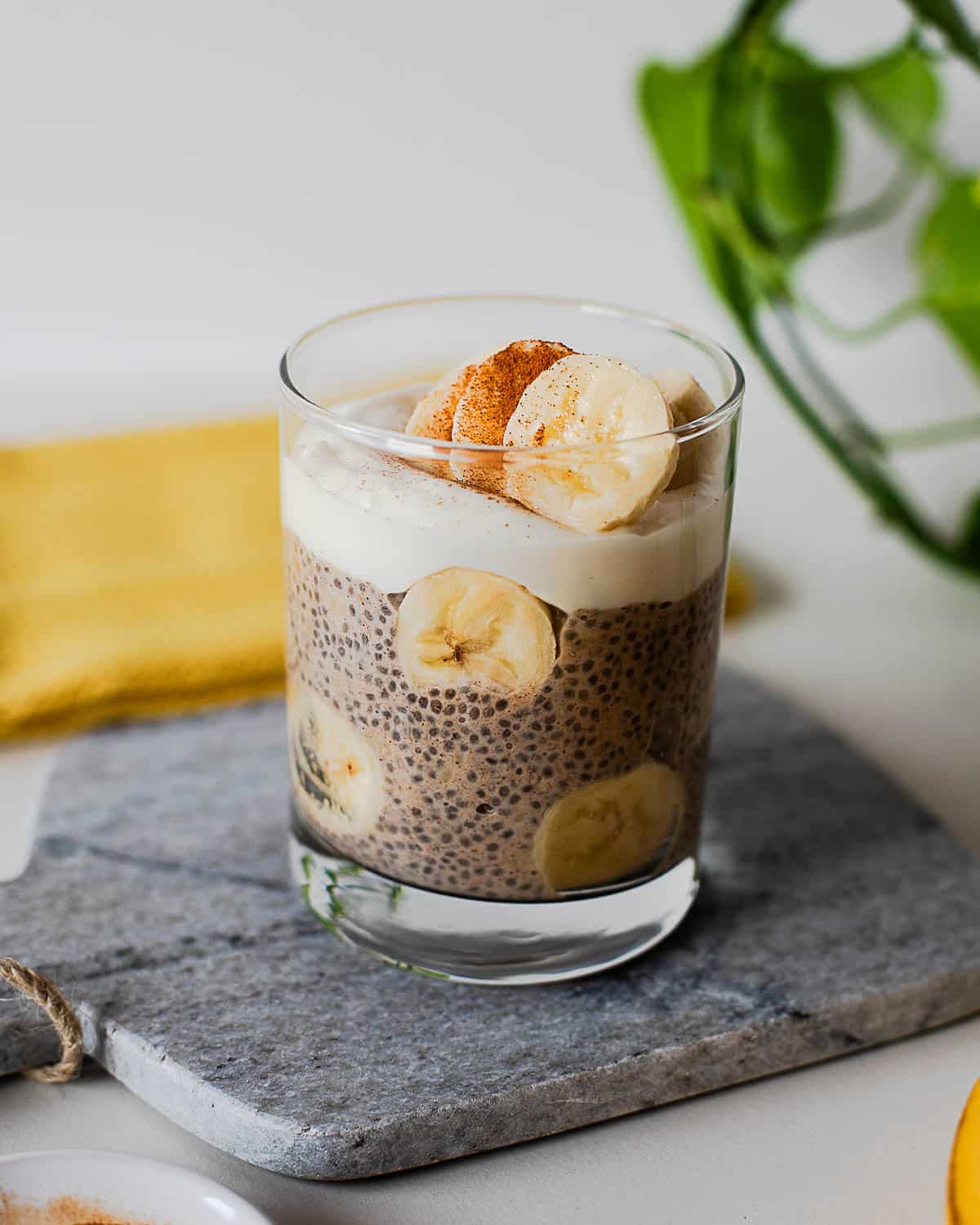 High-protein banana chia pudding with Greek yogurt topping, fresh banana slices, and cinnamon served in a clear glass dish.