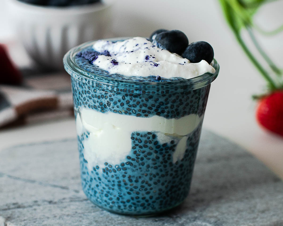 Close-up of creamy blue chia pudding parfait with Greek yogurt, blueberries, and butterfly pea powder garnish.