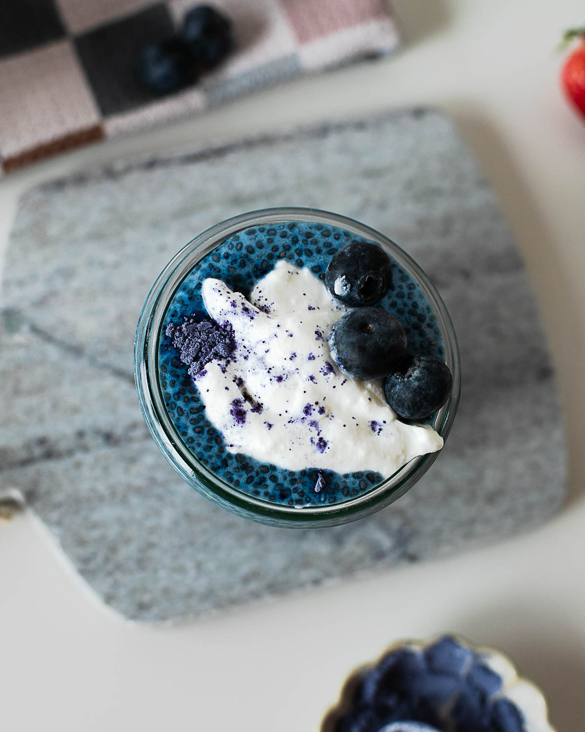 Overhead view of blue chia pudding layered with Greek yogurt and fresh blueberries in a glass jar.
