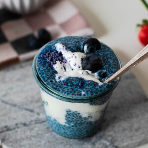 Spoon dipping into a layered blue chia pudding parfait topped with Greek yogurt and fresh blueberries.