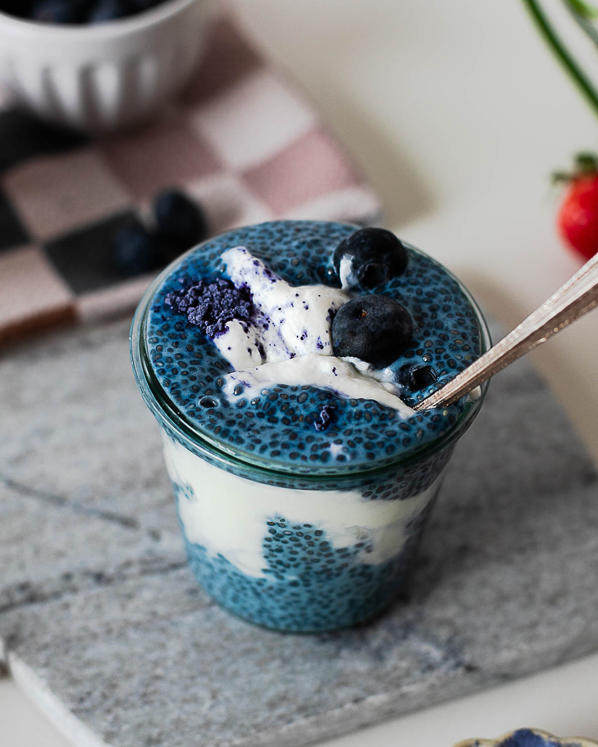 Spoon dipping into a layered blue chia pudding parfait topped with Greek yogurt and fresh blueberries.