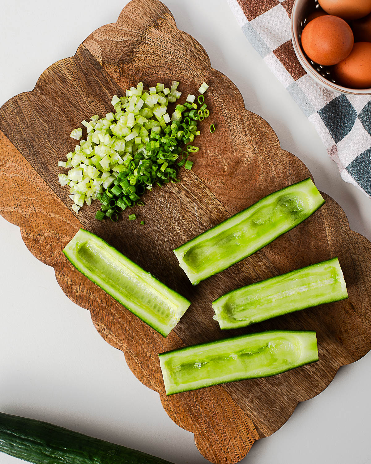 English cucumbers hollowed into boats with the seeds scooped out, alongside chopped celery and green onions, ready for assembling homemade egg salad cucumber boats.