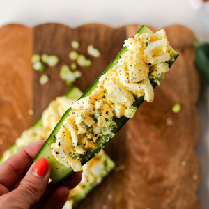 Hand holding a crunchy egg salad cucumber boat loaded with protein-packed egg salad and sprinkled with everything bagel seasoning.