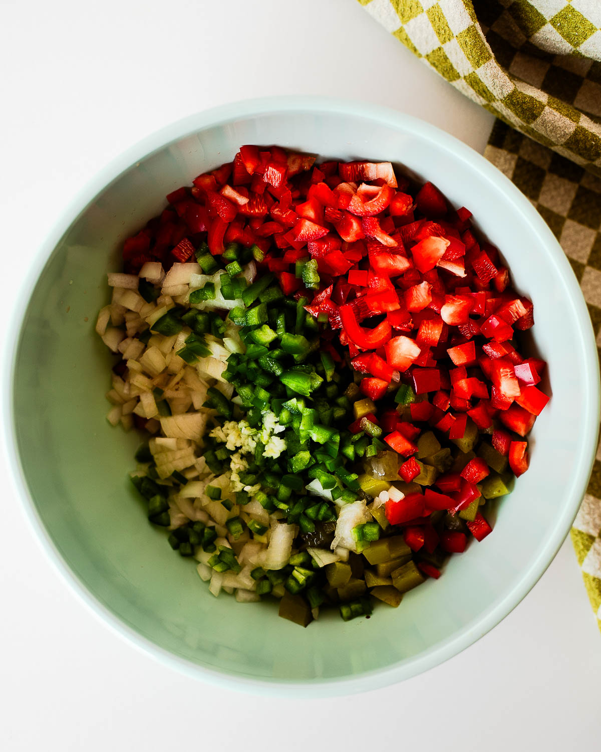 Pickle de gallo ingredients in a light blue mixing bowl, including diced dill pickles, red bell pepper, white onion, jalapeño, garlic, and pickle juice before being mixed together.