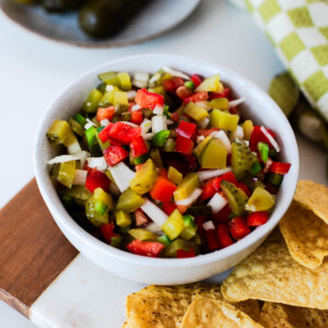 Close-up of pickle de gallo in a white serving bowl surrounded by tortilla chips, showcasing the crunchy vegetables and tangy dill pickles.