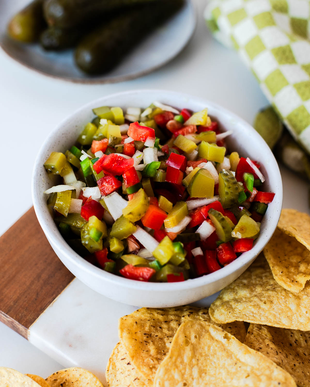 Close-up of pickle de gallo in a white serving bowl surrounded by tortilla chips, showcasing the crunchy vegetables and tangy dill pickles.