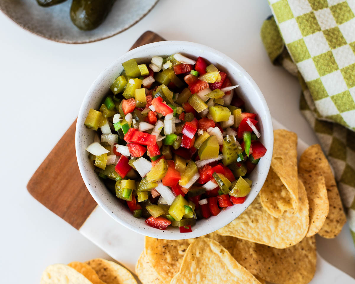 Homemade pickle de gallo served in a white bowl with tortilla chips, featuring crunchy dill pickles, red bell pepper, onion, and jalapeño.