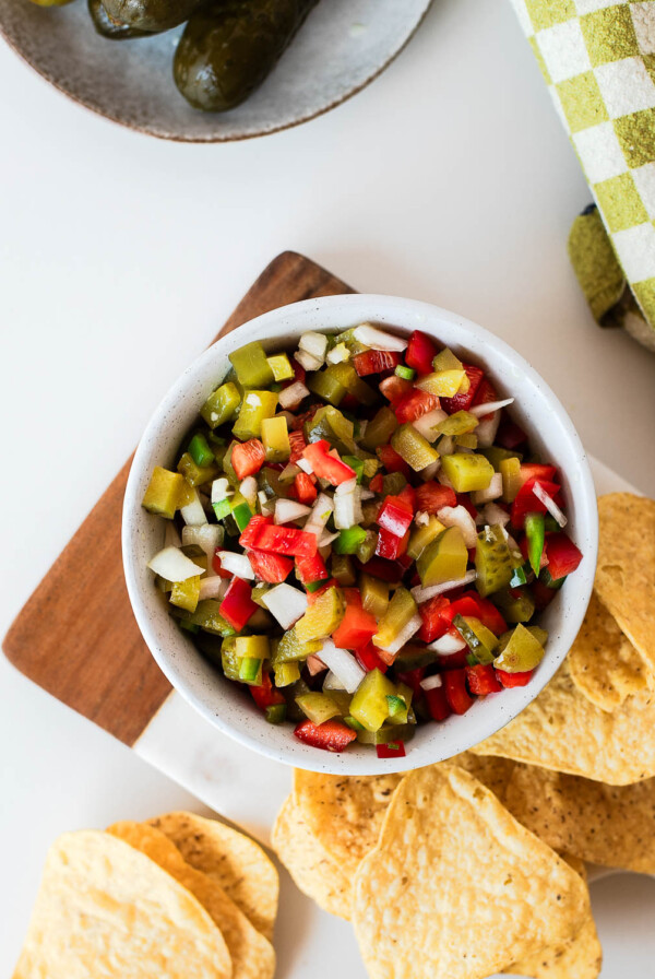 Overhead view of pickle de gallo served with tortilla chips on a wooden board, perfect as a fresh appetizer, dip, or burger topping.