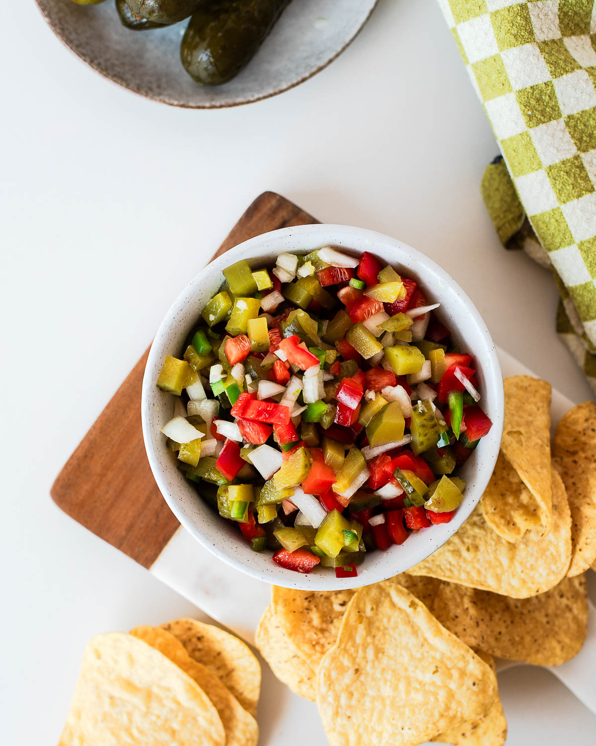 Overhead view of pickle de gallo served with tortilla chips on a wooden board, perfect as a fresh appetizer, dip, or burger topping.