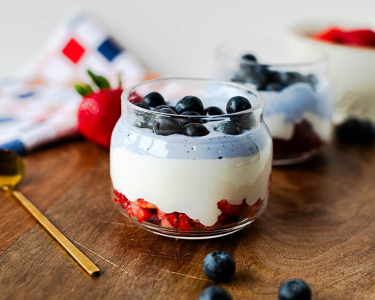 Close-up of a high-protein cottage cheese parfait with layers of strawberries, creamy whipped cottage cheese, naturally blue butterfly pea flower cottage cheese, and fresh blueberries.
