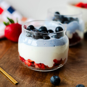 Red, white, and blue cottage cheese parfait layered with fresh strawberries, whipped vanilla cottage cheese, blue cottage cheese, and blueberries in a glass jar.