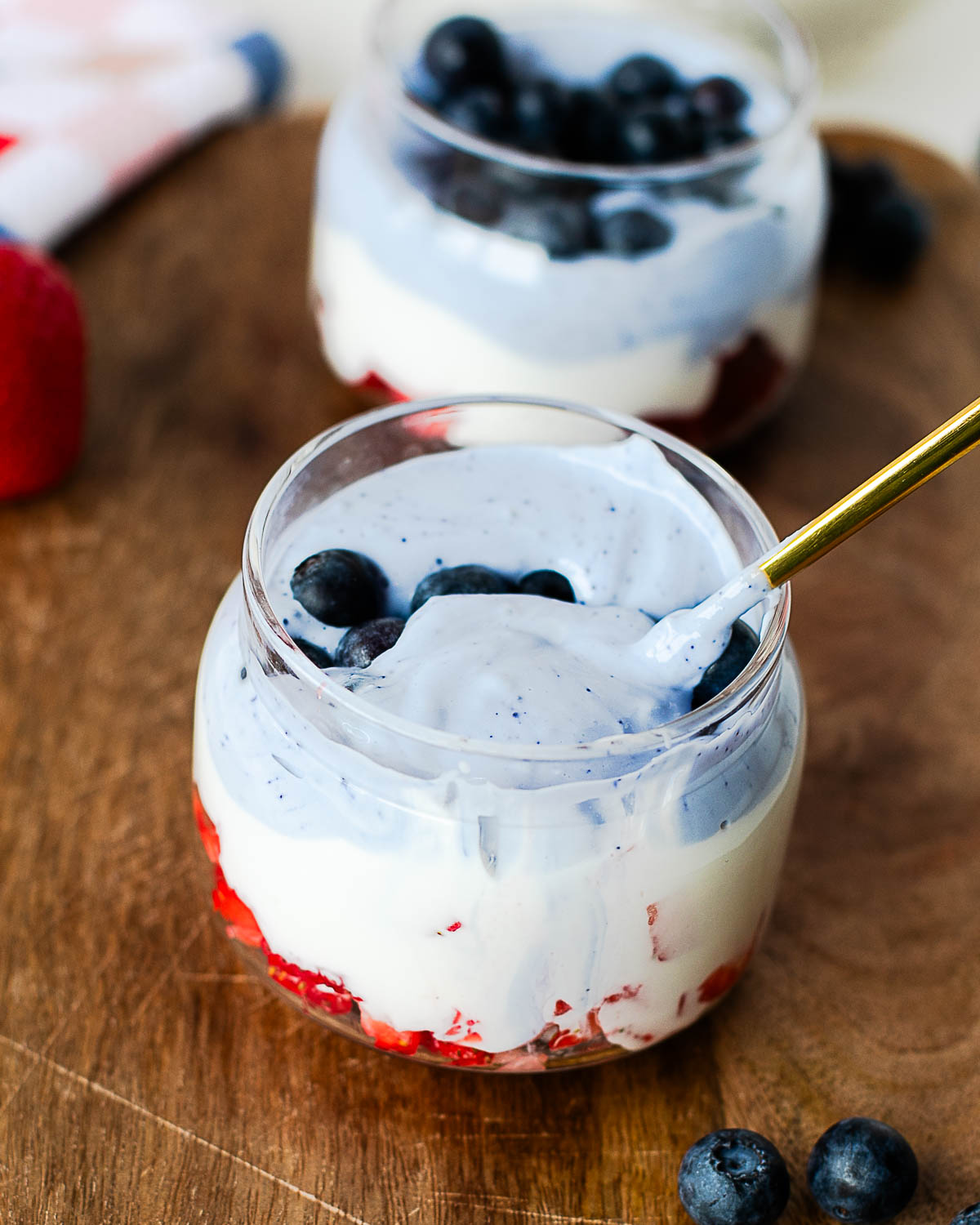 Spoon scooping creamy blue butterfly pea flower cottage cheese from a patriotic parfait layered with strawberries and whipped cottage cheese.