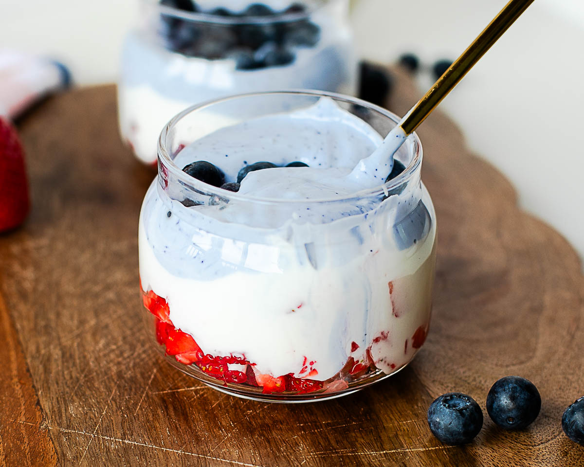 Close-up of a red, white, and blue cottage cheese parfait topped with blueberries and a spoonful of creamy whipped cottage cheese.